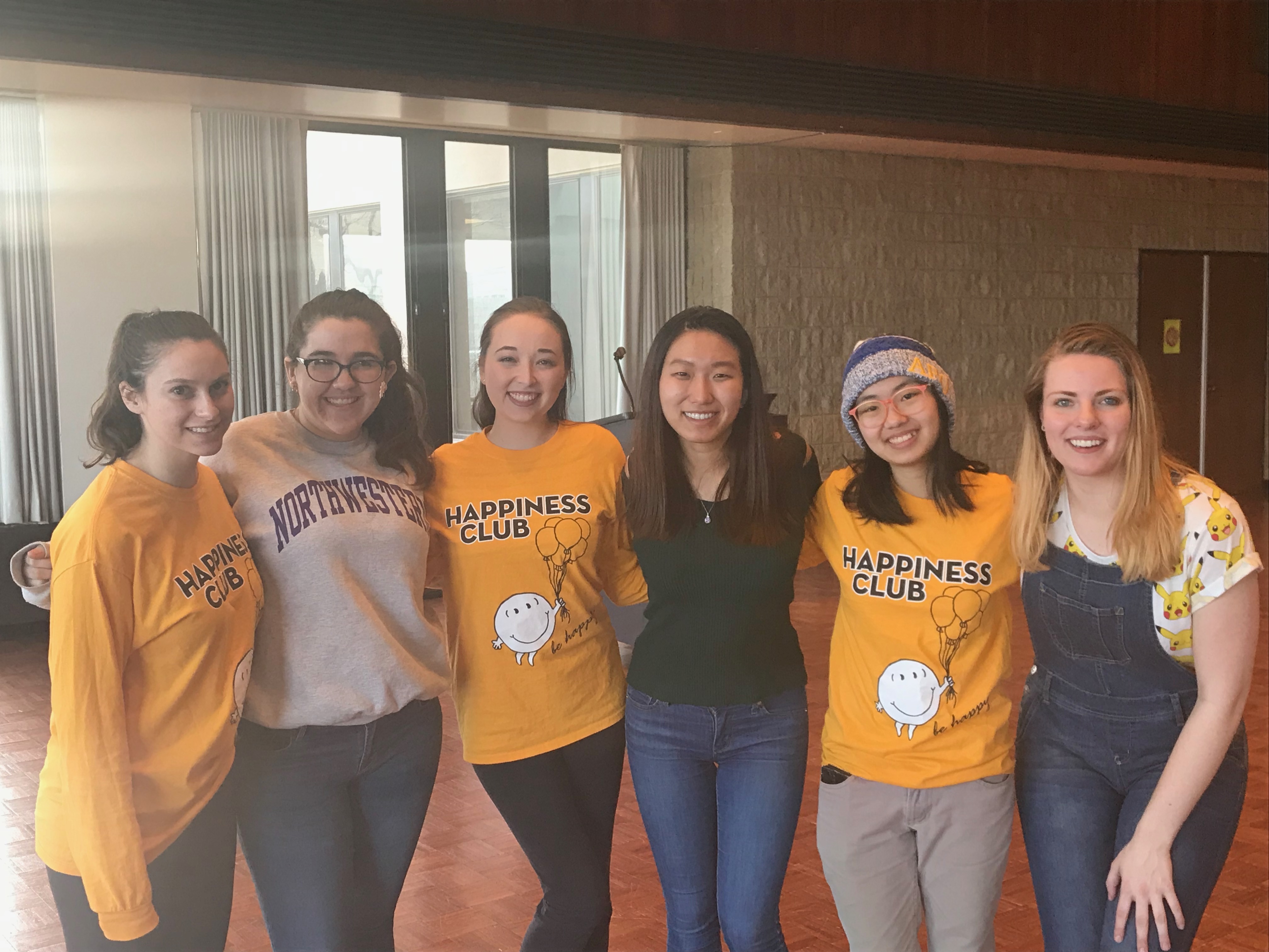 Six girls smile wearing Happiness Club shirts